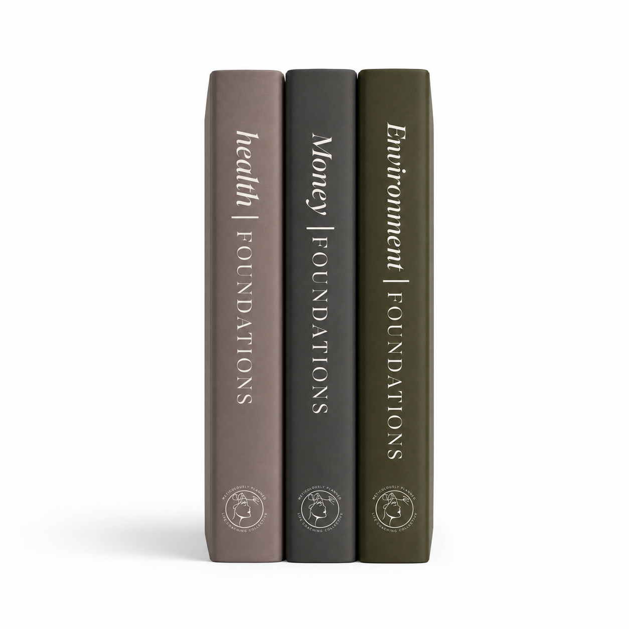 Three slim hardcover books standing upright side by side on a white background. Their spines are colored taupe, charcoal gray, and olive green, with the titles 'health | foundations', 'Money | foundations', and 'Environment | foundations' printed vertically in white, along with small circular logos near the bottom.